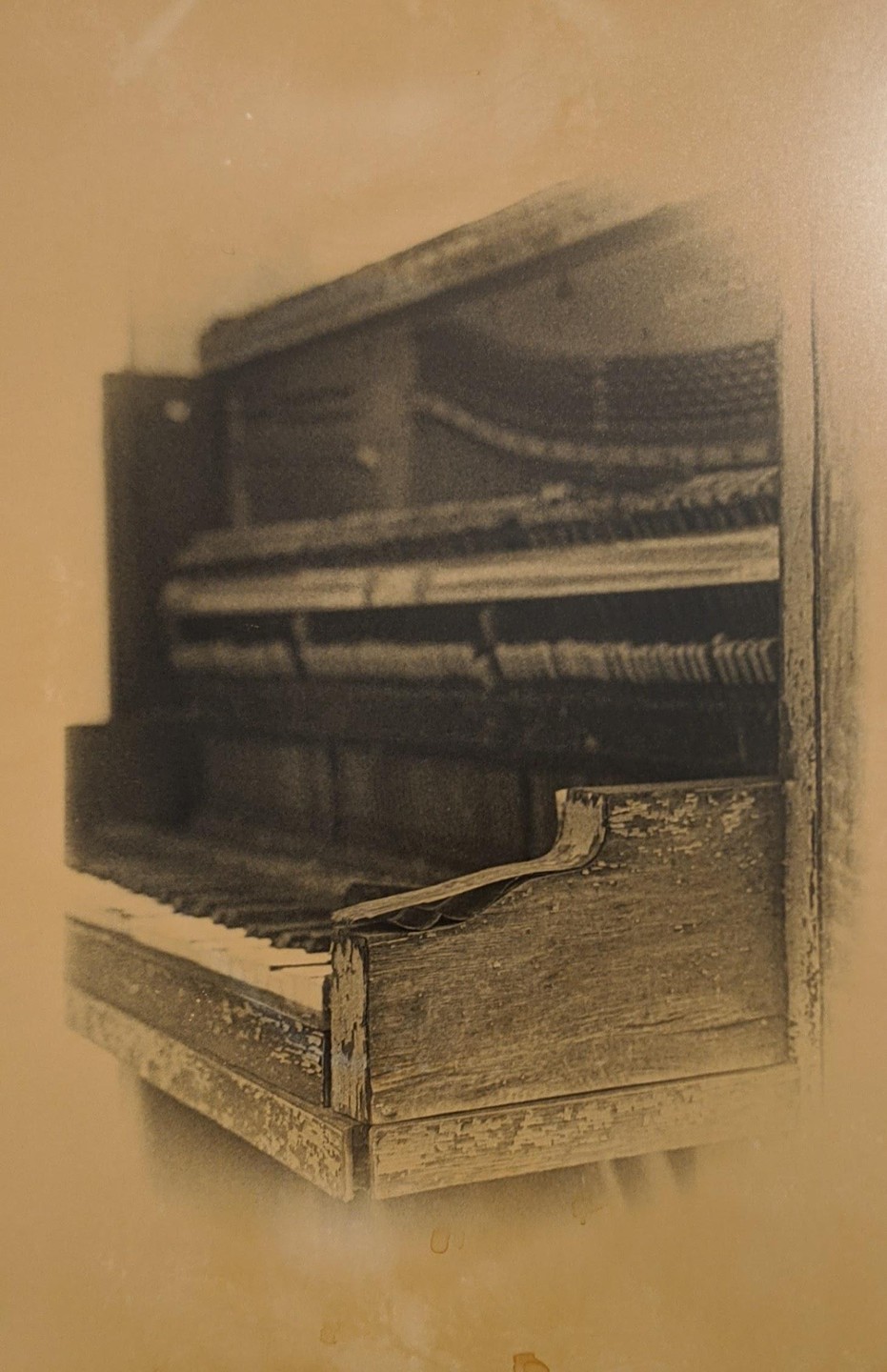 A sepia-toned image shows a close-up of an old, damaged piano with exposed hammers and strings.