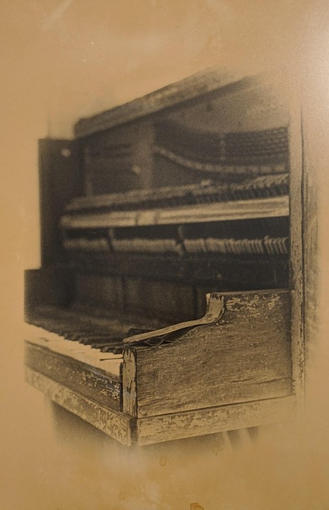 A sepia-toned image shows a close-up of an old, damaged piano with exposed hammers and strings.