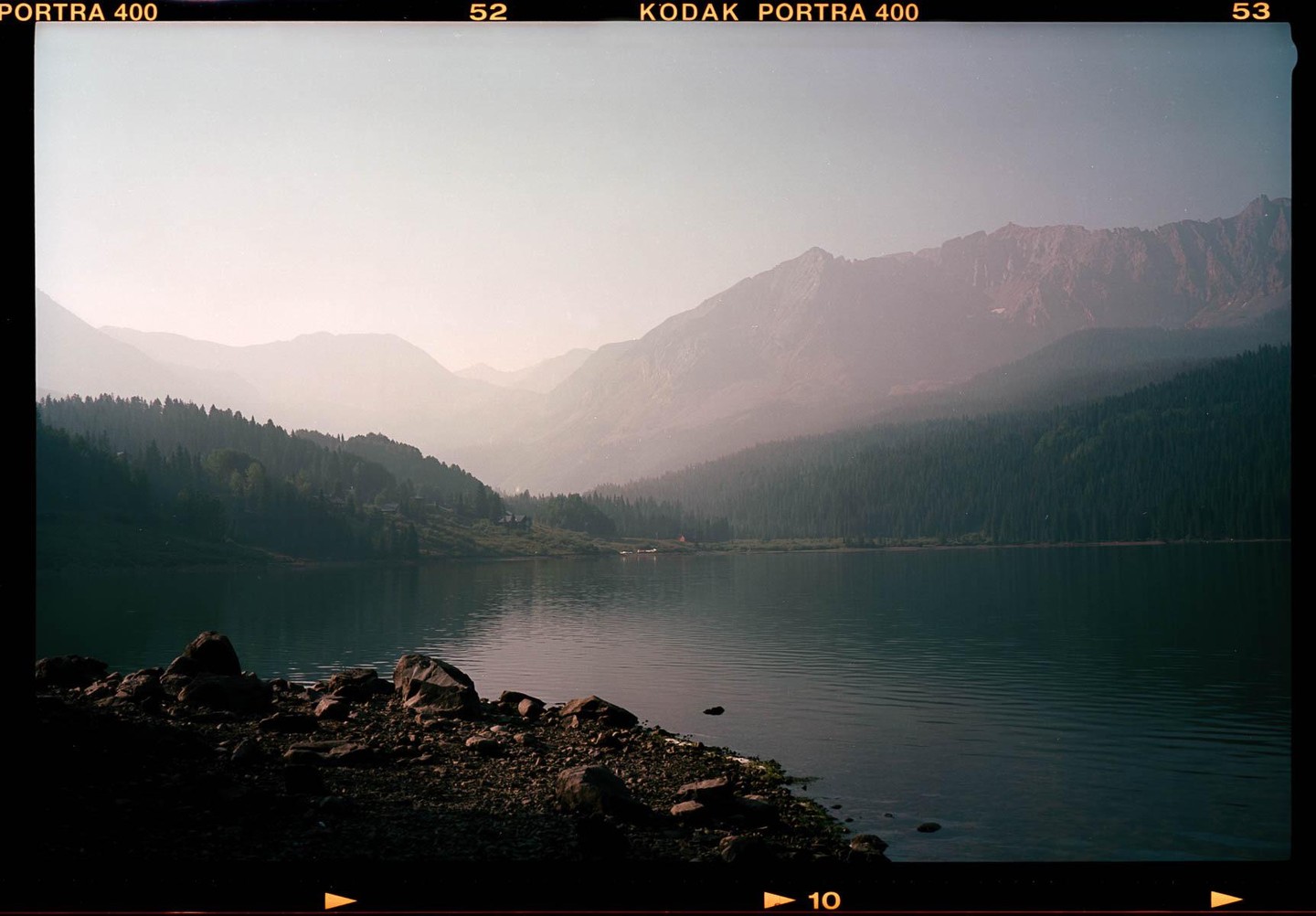 A hazy mountain lake is surrounded by a forest and rocky shore.