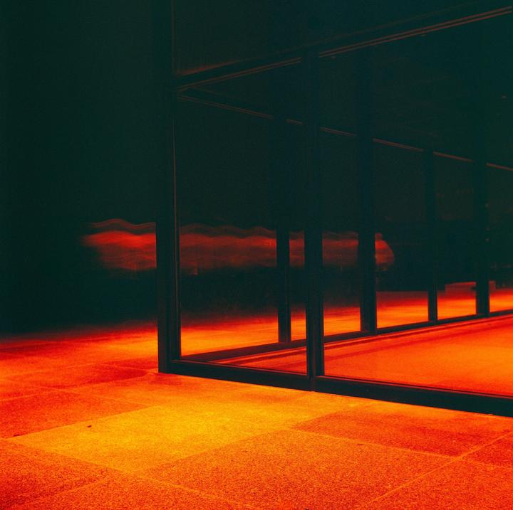 A dark room with a tiled floor is illuminated by a strong red light, reflecting in a glass partition.