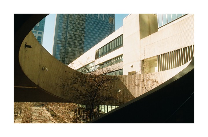 A modern building with a curved concrete walkway is framed by a dark, curved structure in the foreground.