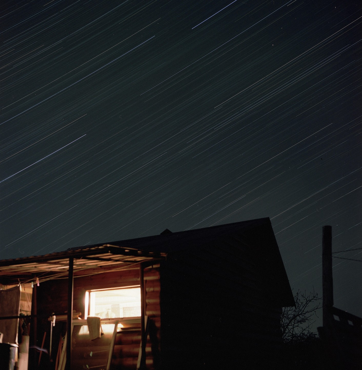 A long exposure photograph captures star trails above a building with a single illuminated window at night.