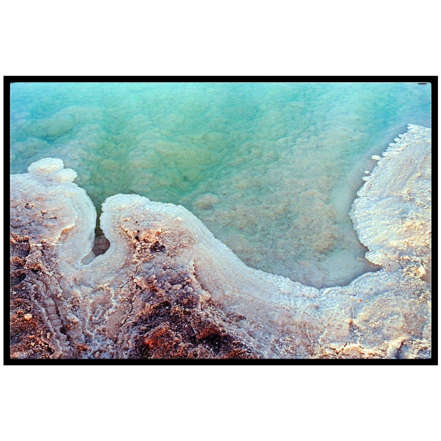 A body of turquoise water meets a textured, salt-encrusted shoreline.