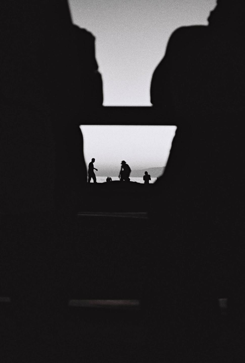 Three people are silhouetted against the ocean and sky, framed by dark shapes in the foreground.