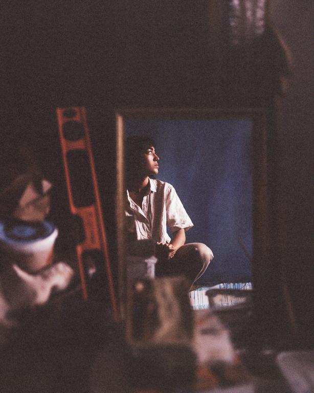 A man crouches in a dimly lit room, looking up and to the right.