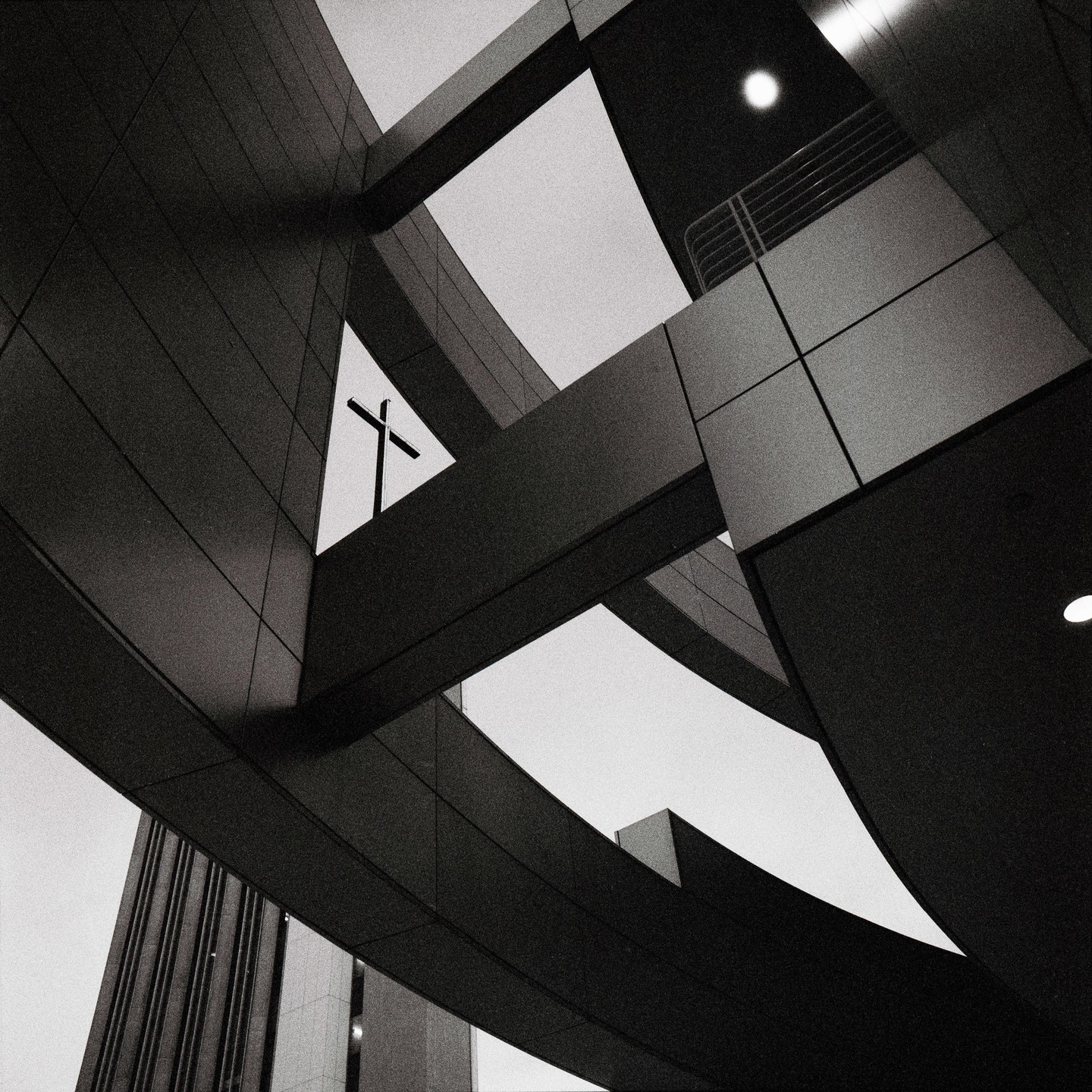 A cross is visible through a triangular opening in a modern building.