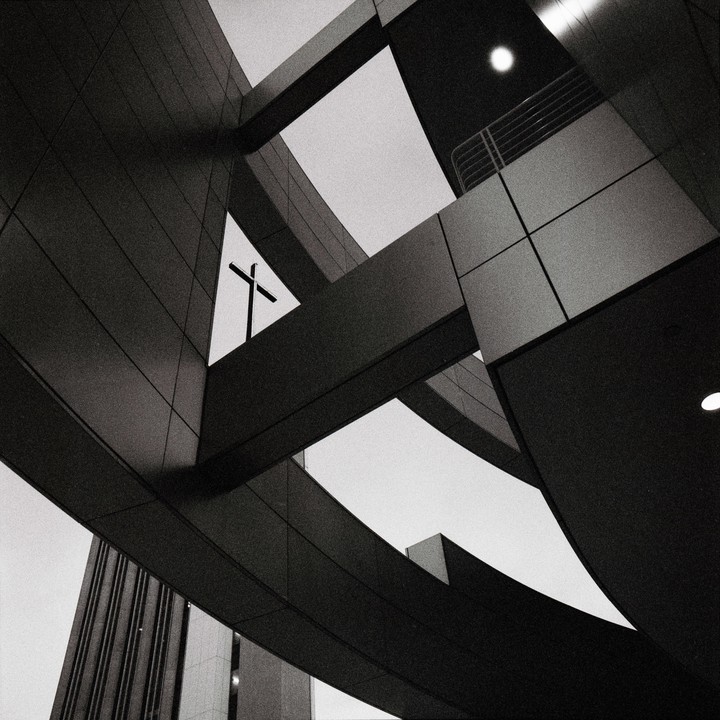 A cross is visible through a triangular opening in a modern building.