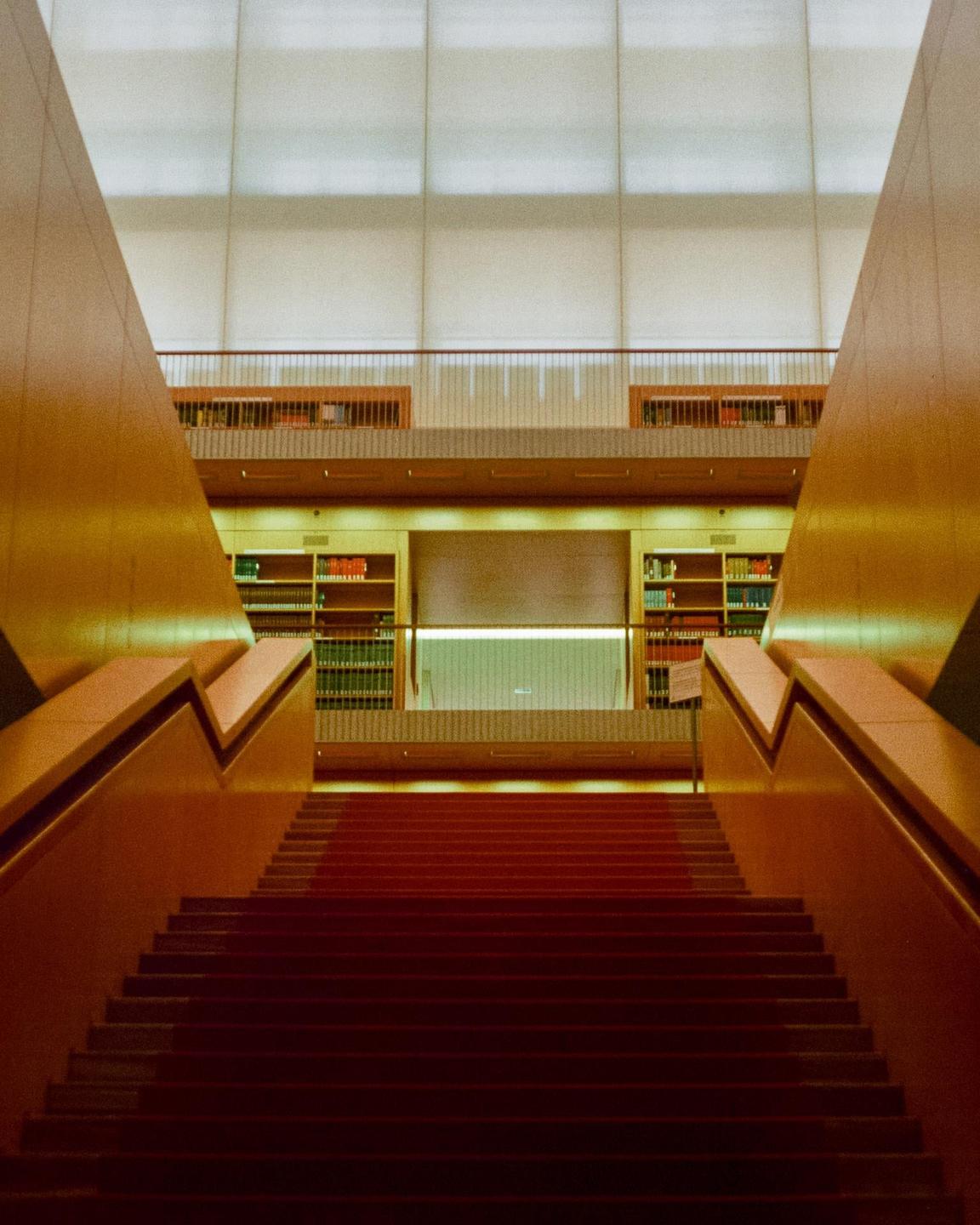 A red carpeted staircase leads up to a library with bookshelves and a balcony.