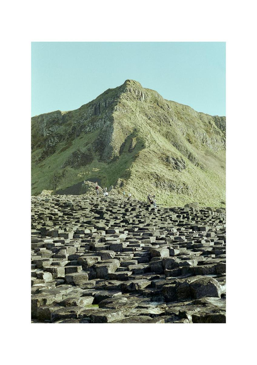 A mountain rises above a field of hexagonal rock columns with people walking among them.