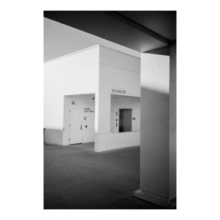 A black and white photograph shows a building with an elevator and stairs.