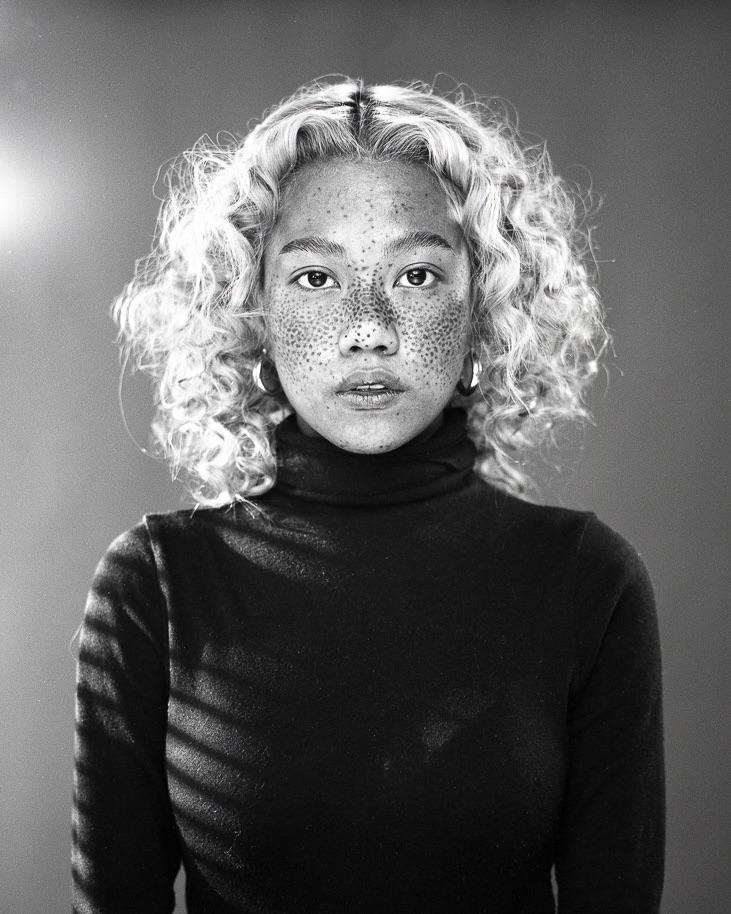 A woman with curly hair and freckles wears a turtleneck and hoop earrings.