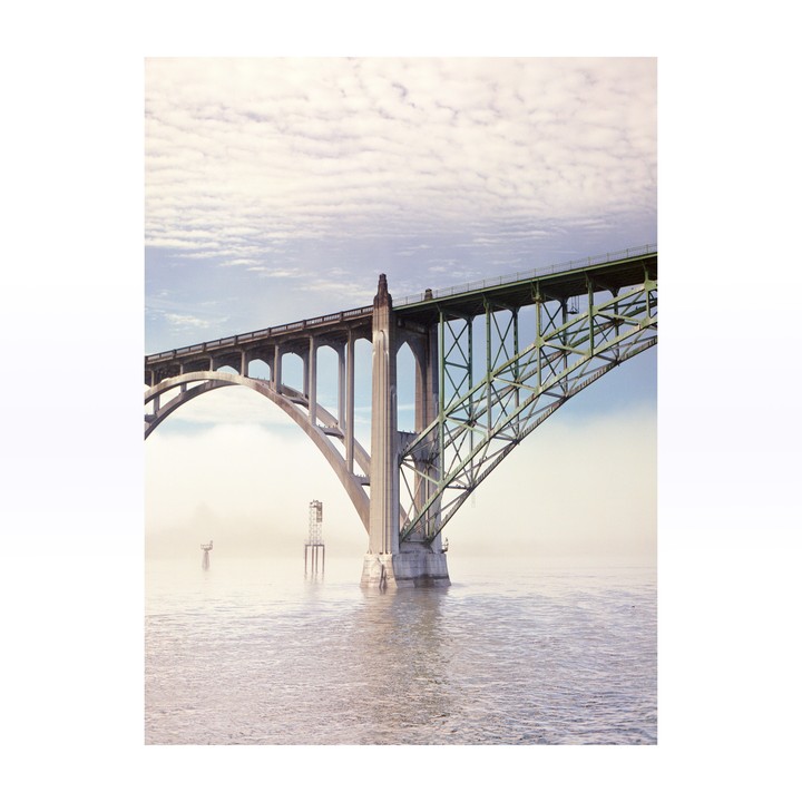 A large concrete and steel bridge spans across a body of water under a cloudy sky.