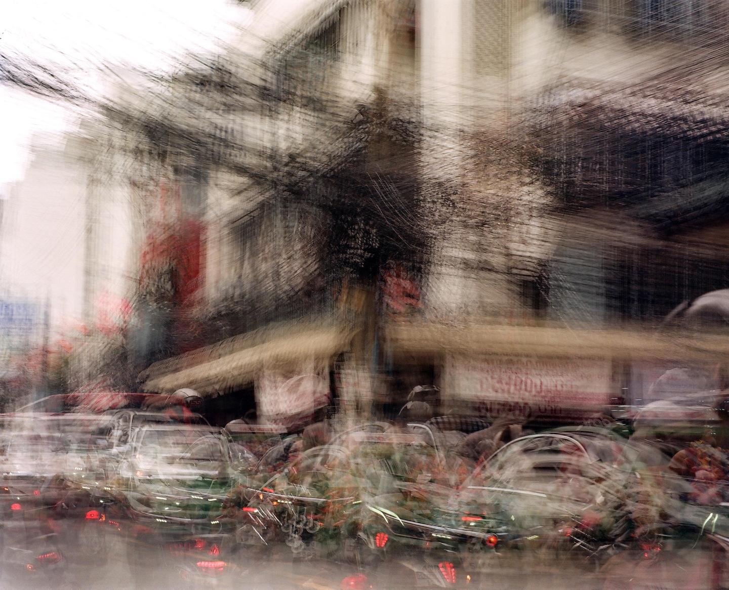 A street scene is blurred by motion, showing buildings and vehicles with red lights.