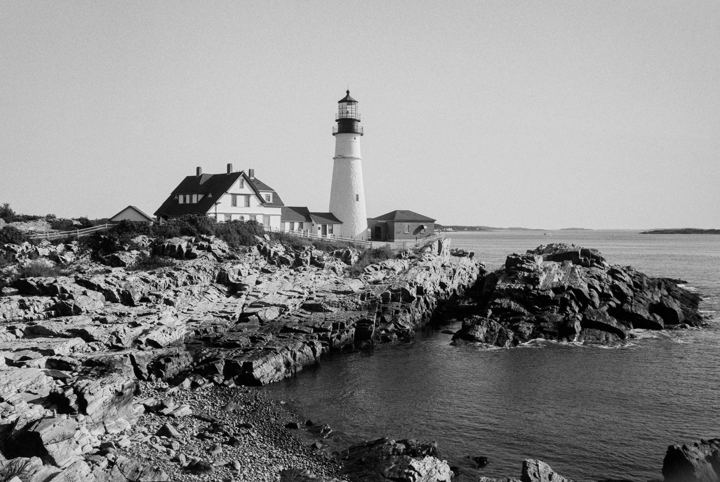 A lighthouse and a house stand on a rocky coast overlooking the ocean.