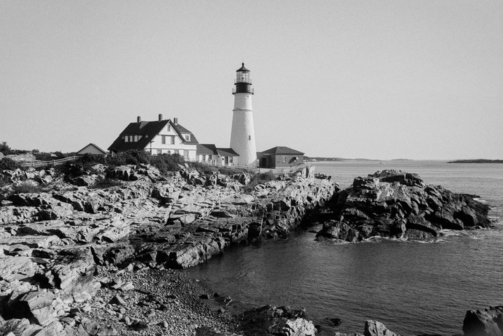 A lighthouse and a house stand on a rocky coast overlooking the ocean.