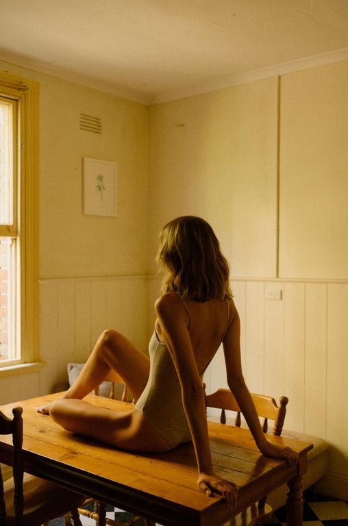 A woman in a leotard sits on a wooden table in a room with yellow walls.