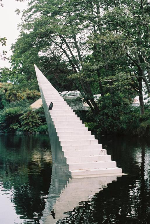 A bird sits on a long white staircase that extends into a body of water surrounded by trees.