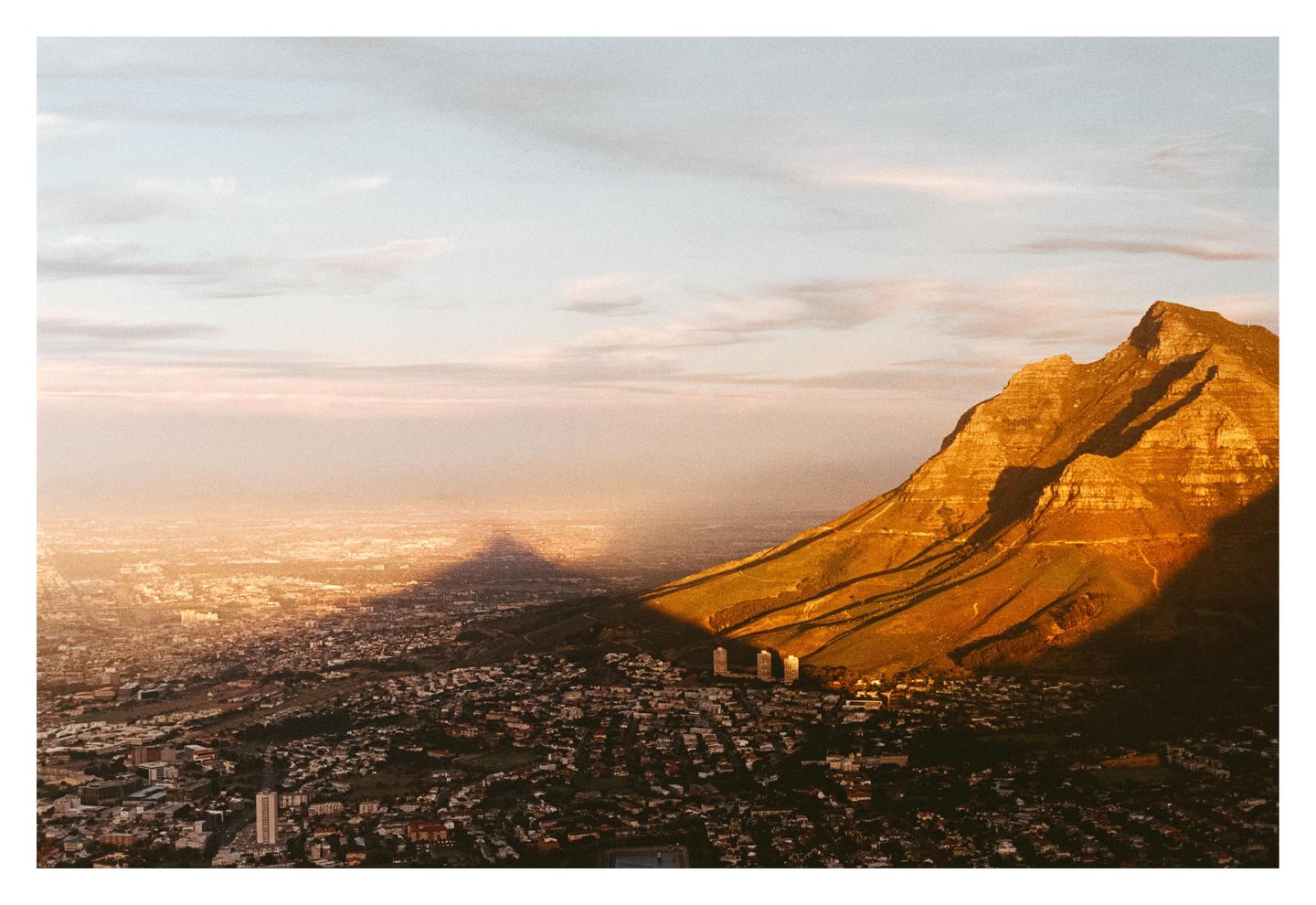 A mountain casts a large shadow over a city at sunset.