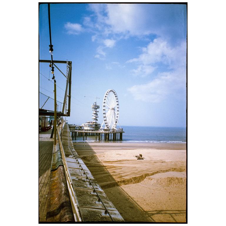 A ferris wheel and a tower stand on a pier over the ocean next to a sandy beach.