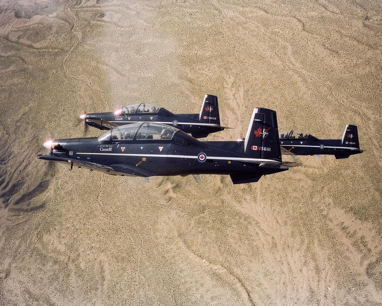 Three dark blue airplanes fly in formation over a desert landscape.