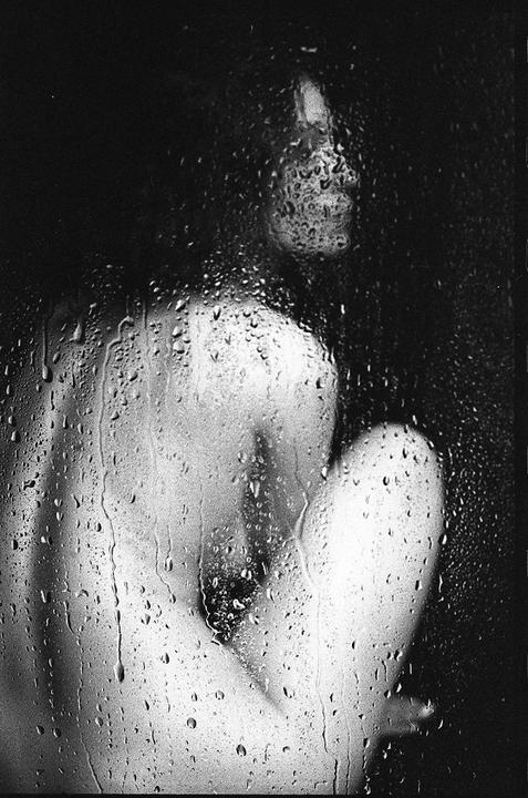 A person is visible through a wet glass surface covered in water droplets.