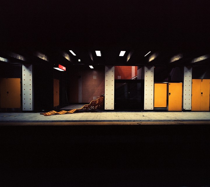 An empty subway platform features yellow doors, tiled pillars, and a collapsed orange barrier.