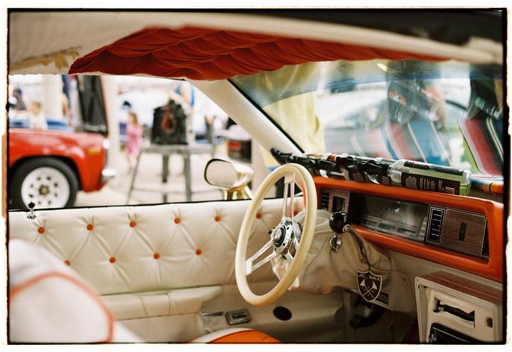 The interior of a customized car with white upholstered seats and an orange dashboard is visible from the driver's side.
