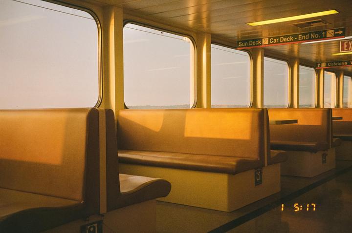 The interior of a ferry shows rows of empty seats and windows looking out onto a hazy sky.
