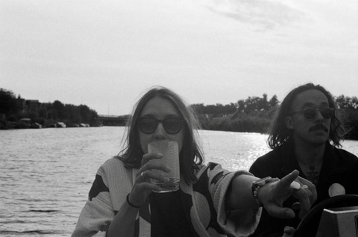 A woman drinks from a glass while a man points forward on a boat.