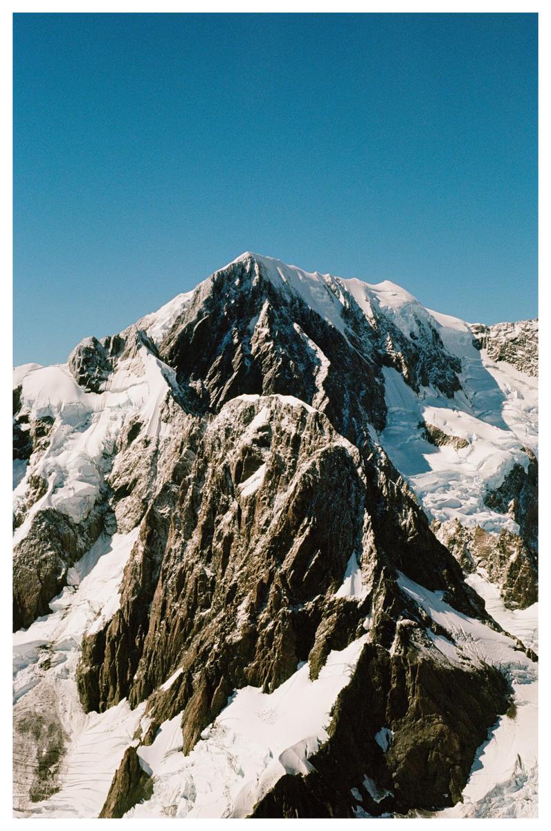 A snow-capped mountain peak rises against a clear blue sky.