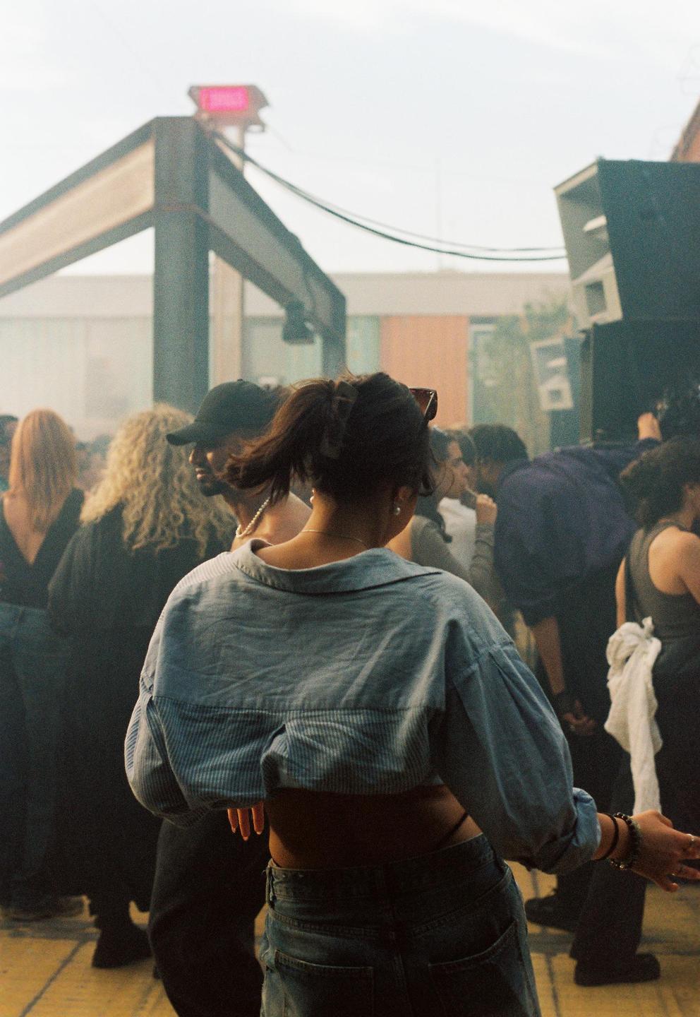 A woman with her back to the camera dances in a crowd of people.