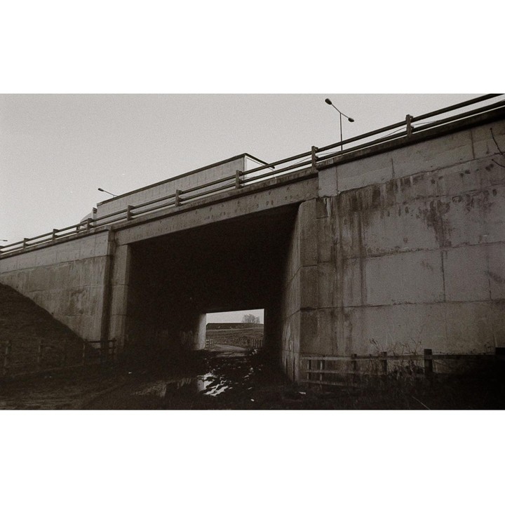 A concrete overpass with a dark tunnel and muddy ground is visible under a gray sky.