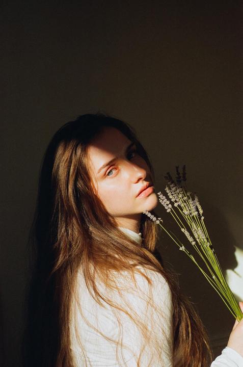 A woman with long hair holds a bunch of lavender flowers while looking over her shoulder.