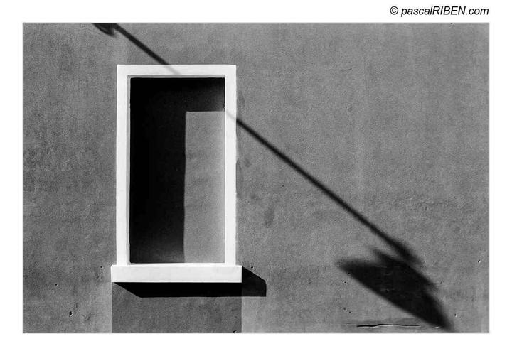 A window with a shadow of a pole and its reflection on a wall.