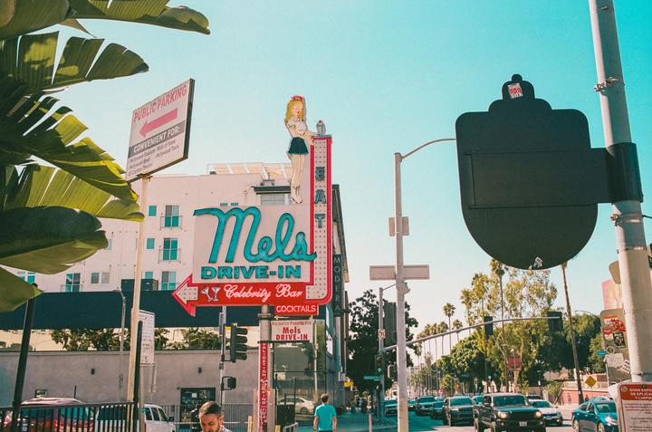 A street view shows a large neon sign for Mel's Drive-In with a woman holding a tray on top, and cars are visible on the street.