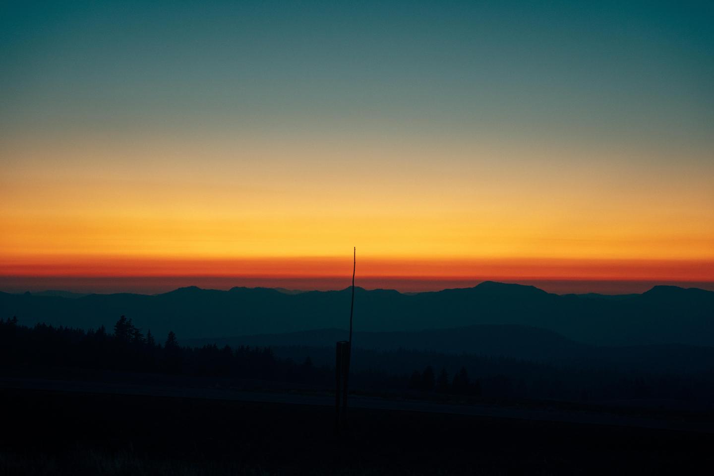 A single pole stands in front of a mountain range at sunset.