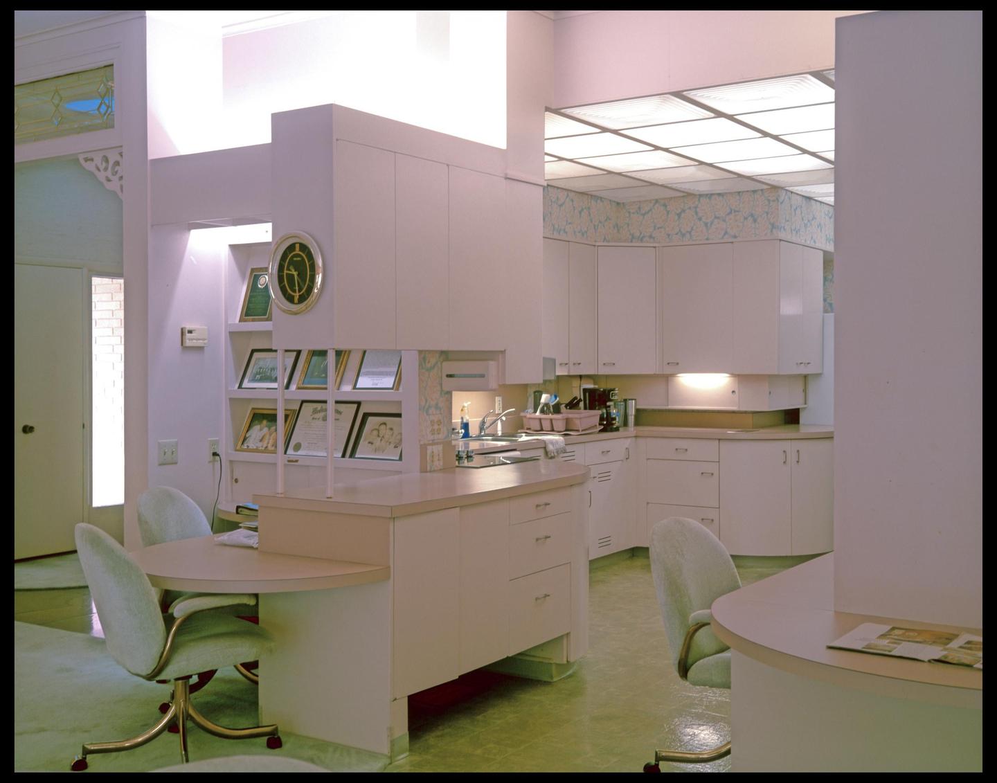 A 1960s kitchen with white cabinets, a drop ceiling, and a small dining area is shown.