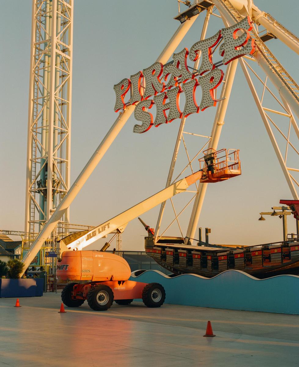 An orange lift is parked next to a pirate ship ride with a "Pirate Ship" sign above it.