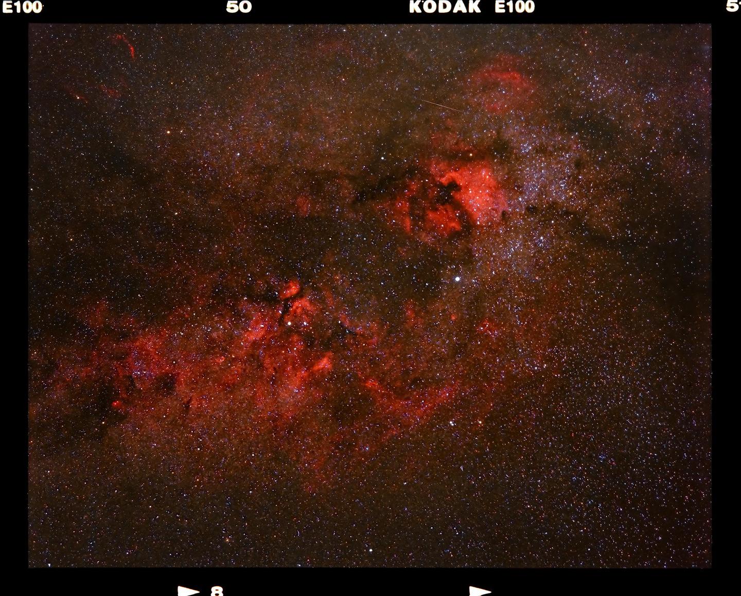 A dark sky is filled with countless stars and red interstellar hydrogen clouds.