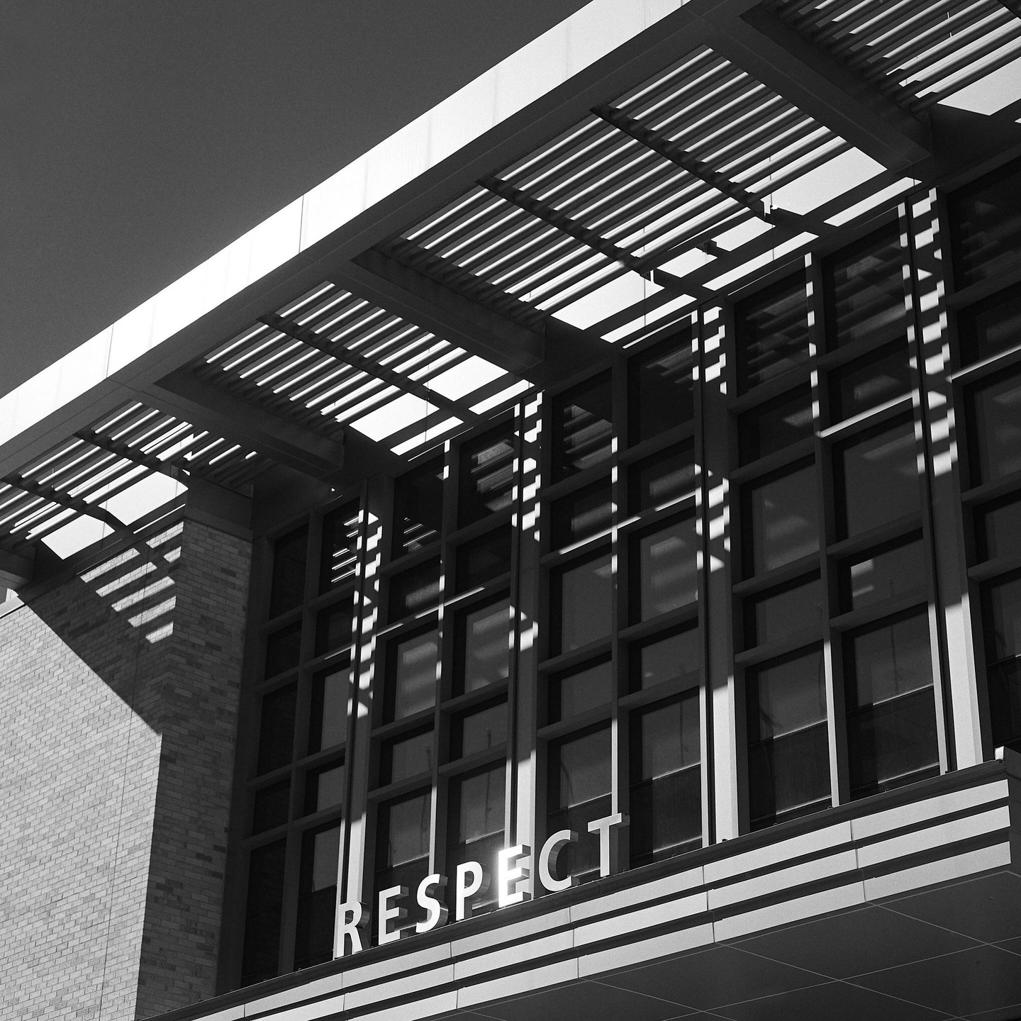 The word "RESPECT" is visible on the facade of a building with strong shadows from an overhang.