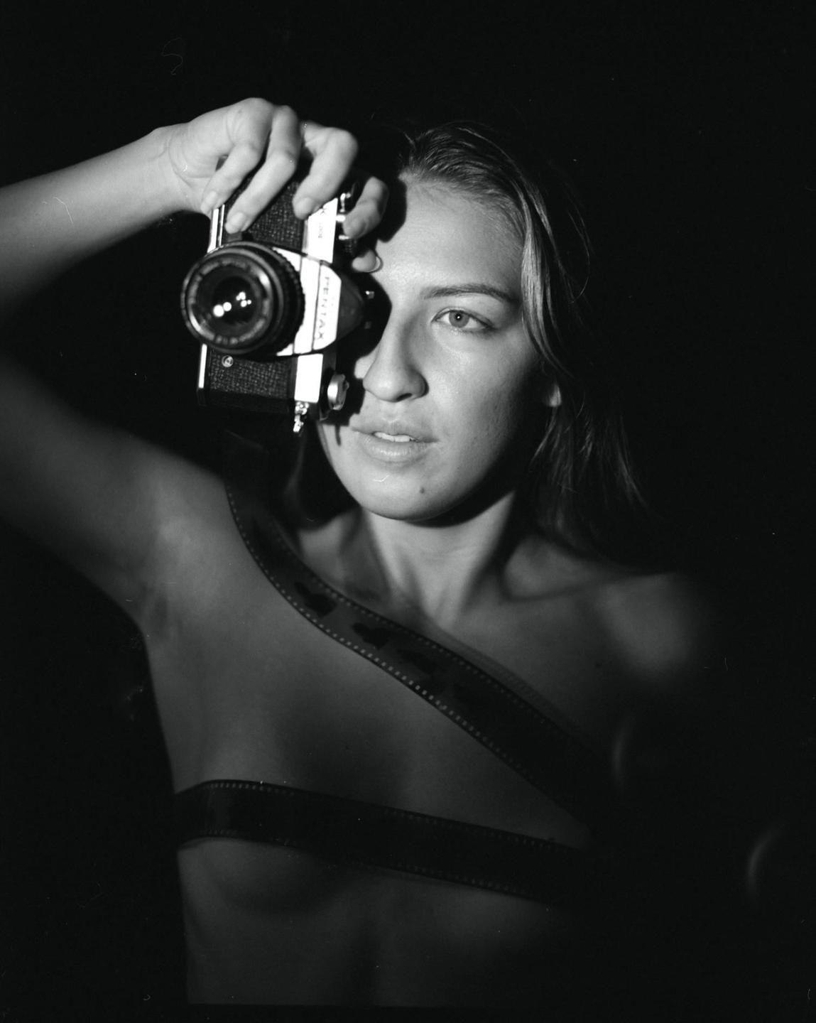 A woman holds a camera to her eye while film strips are wrapped around her body.