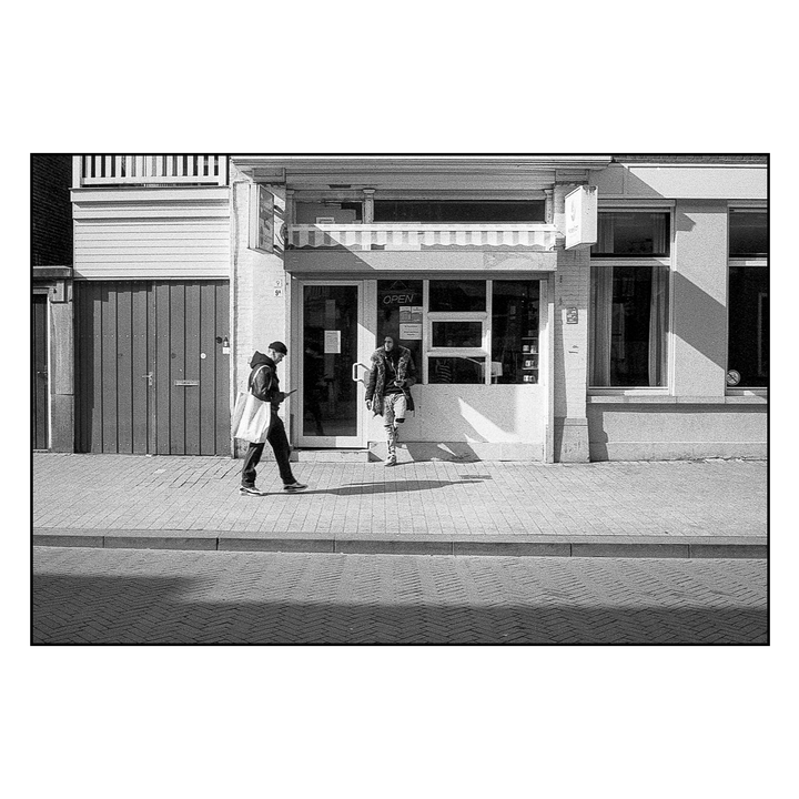 A man walks past a storefront with another man standing in the doorway.