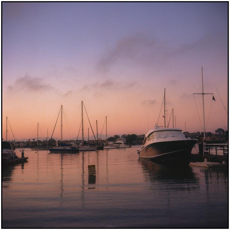A marina at sunset shows several boats docked in the water with a colorful sky above.