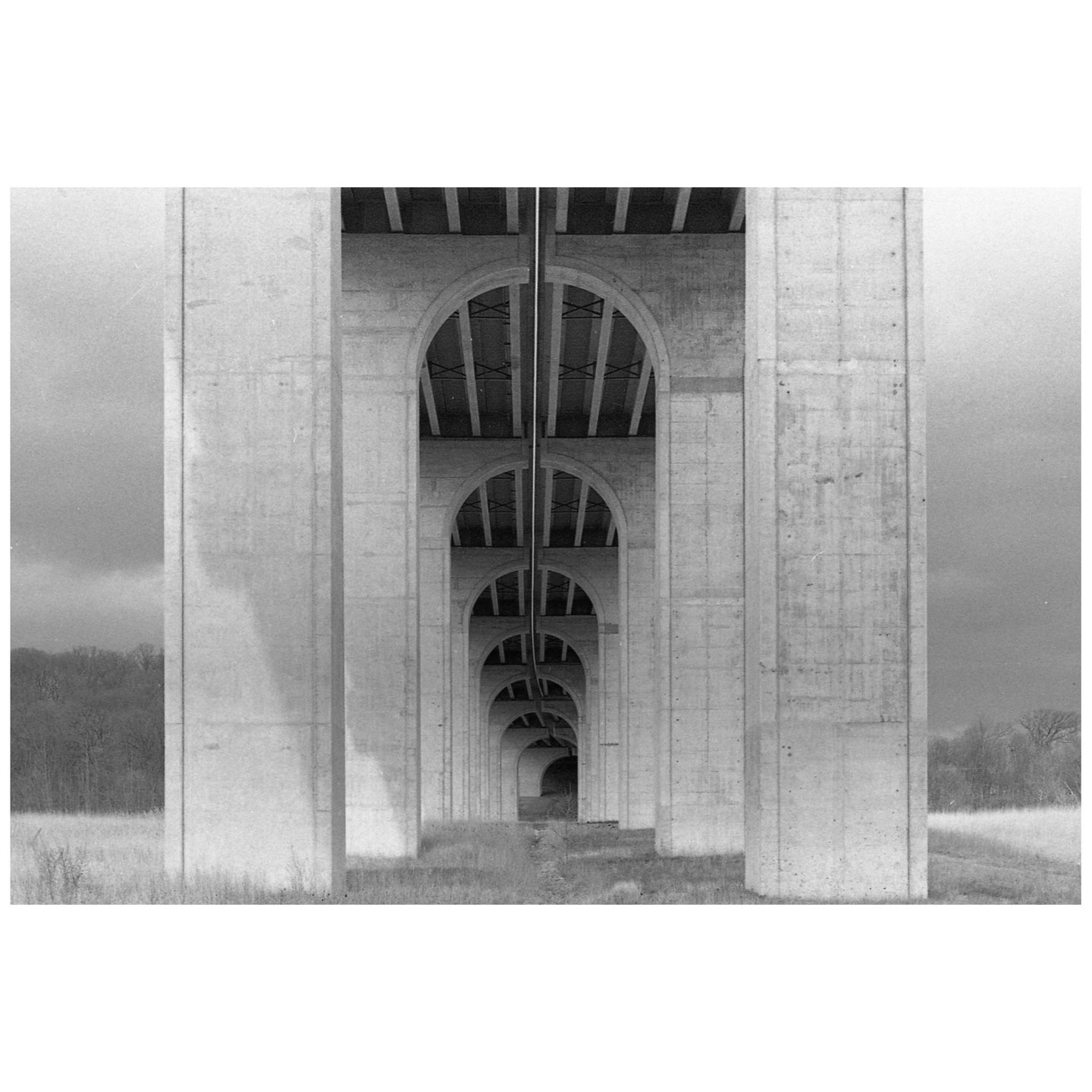 A long row of concrete arches supporting a bridge extends into the distance over a grassy field.