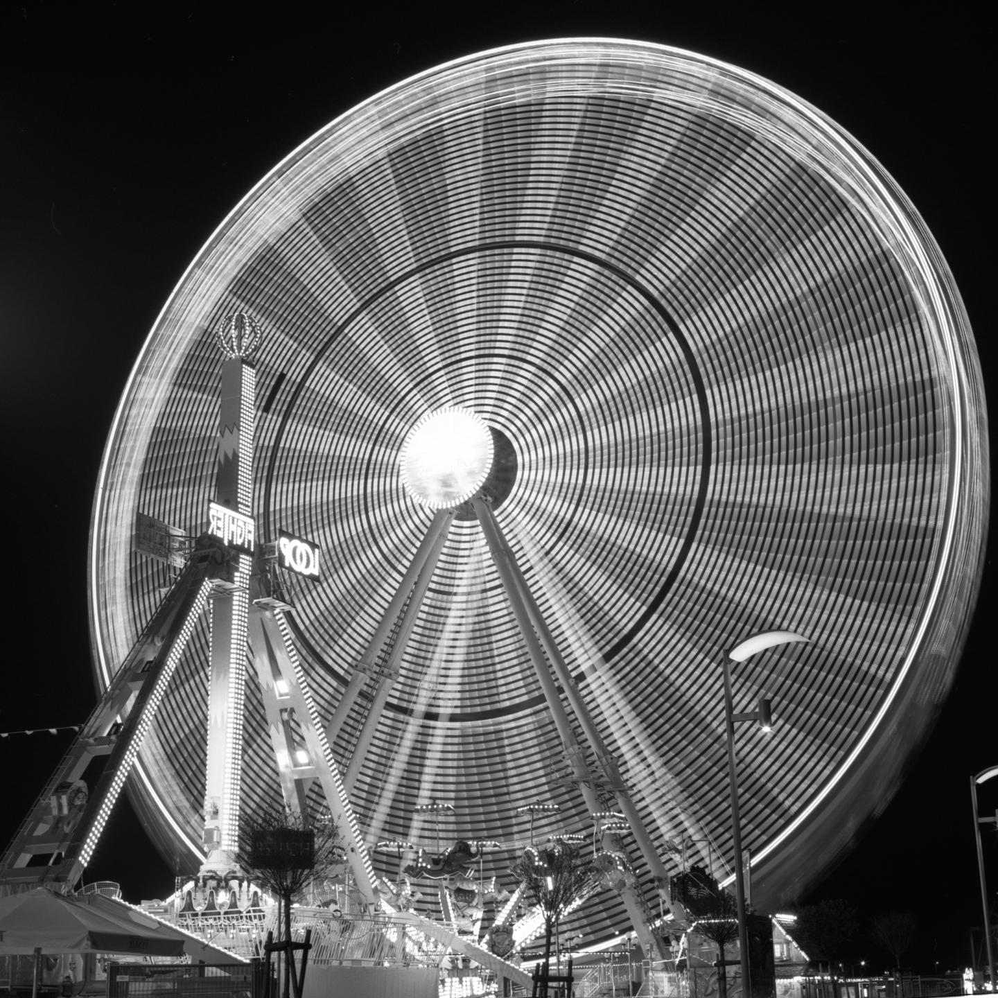 A long exposure captures the motion of a ferris wheel at night.