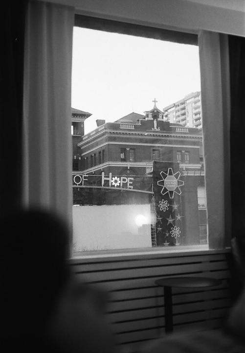 A building with a cross on its roof and a banner that reads "OF HOPE" is visible through a window with curtains.