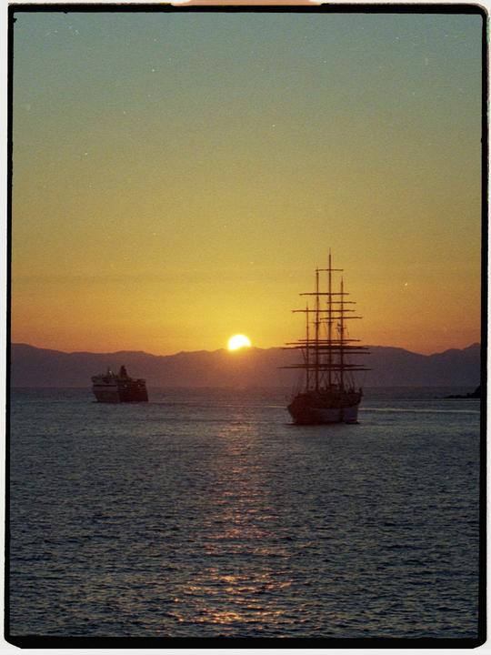 Two ships are silhouetted against a sunset over mountains.