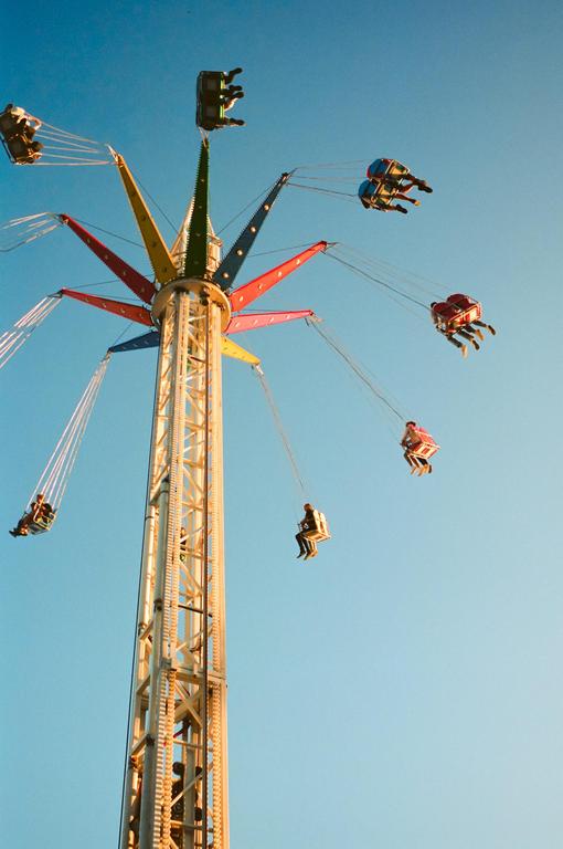 People ride a colorful swing ride against a clear blue sky.