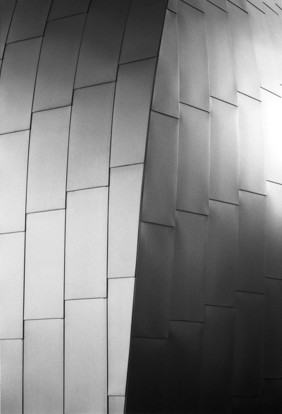 A black and white abstract image shows a building facade with curved, rectangular panels.