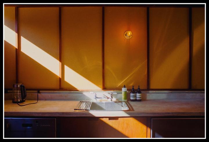 Sunlight streams across a kitchen counter with a sink, kettle, and bottles.